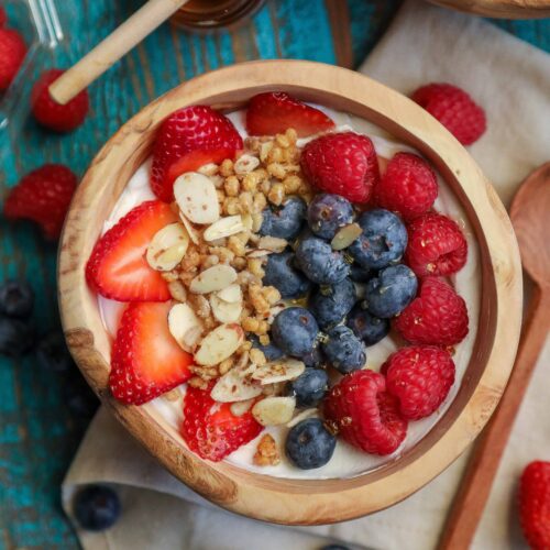 Flat lay shot of a wooden bowl with yogurt topped with granola and fresh berries.