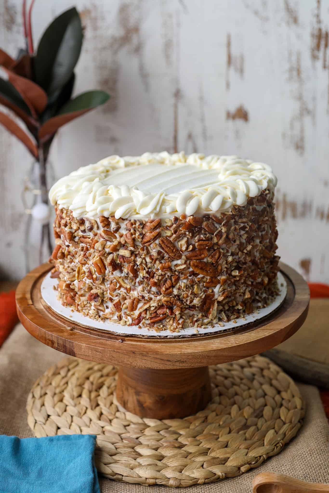round carrot cake wrapped with pecans on a wooden cake stand